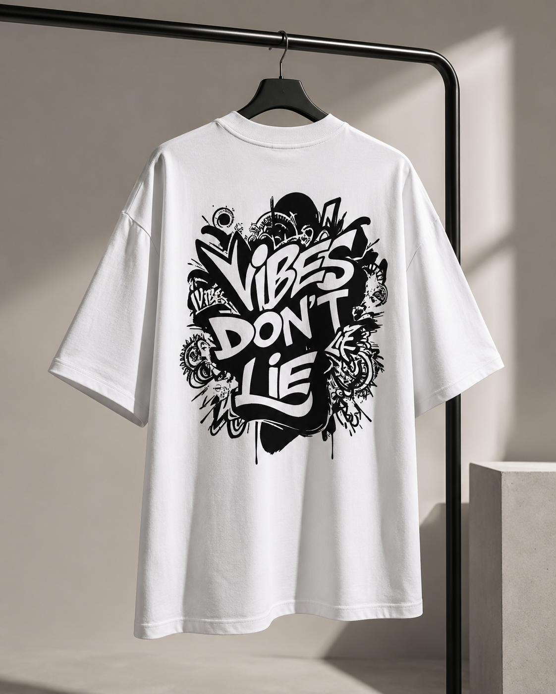 White oversized Vibes Don’t Lie t-shirt hanging on a black clothing rack with black back print.